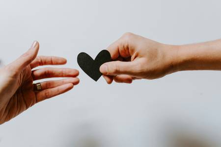 Quelle: unsplash.com / Kelly Sikkema, https://unsplash.com/de/fotos/person-die-schwarzes-herz-ausschnittpapier-erreicht-XX2WTbLr3r8 jemand reicht ein Herz an anderen