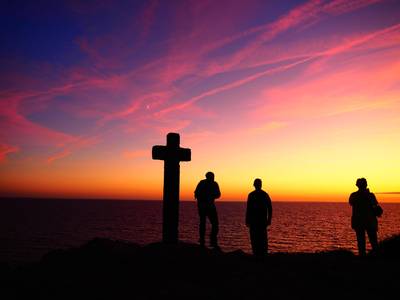 Quelle: Pfarrbriefservice.de, Pixabay.com / dozemode, https://www.pfarrbriefservice.de/image/menschen-und-kreuz Menschen stehen bei Kreuz vor Sonnenuntergang